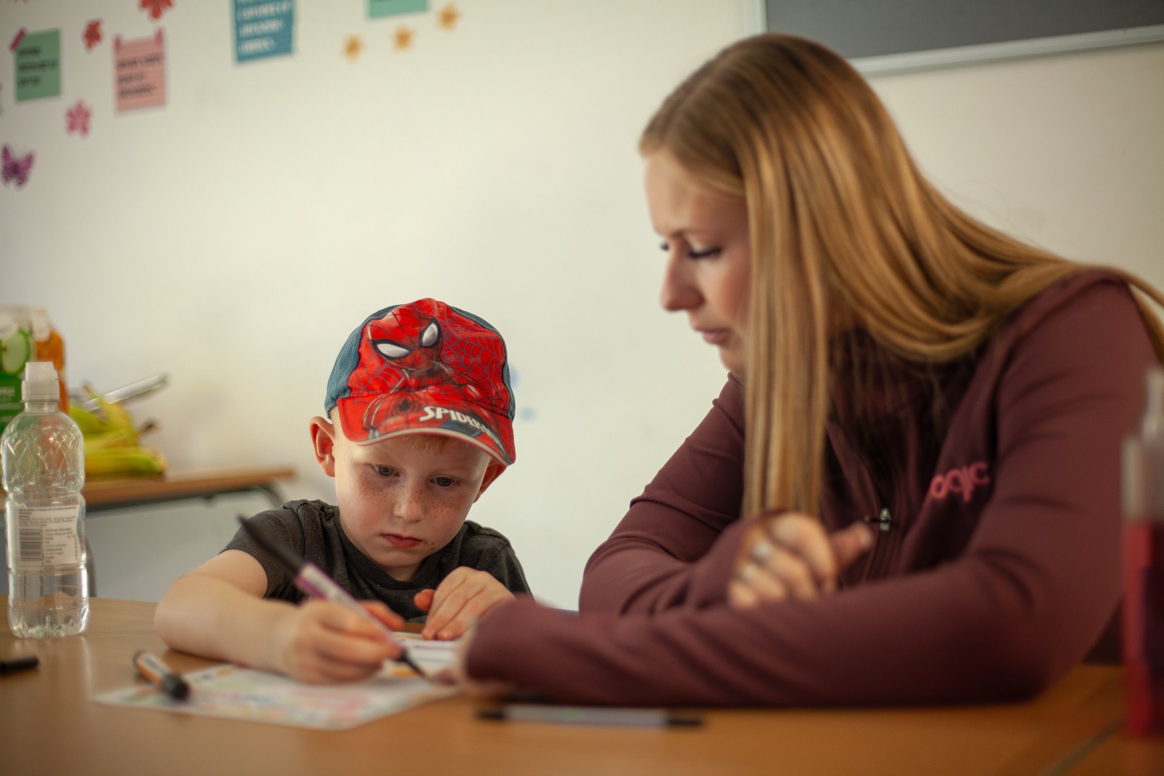 A Nulogic practitioner helps a young boy with his writing at a table.